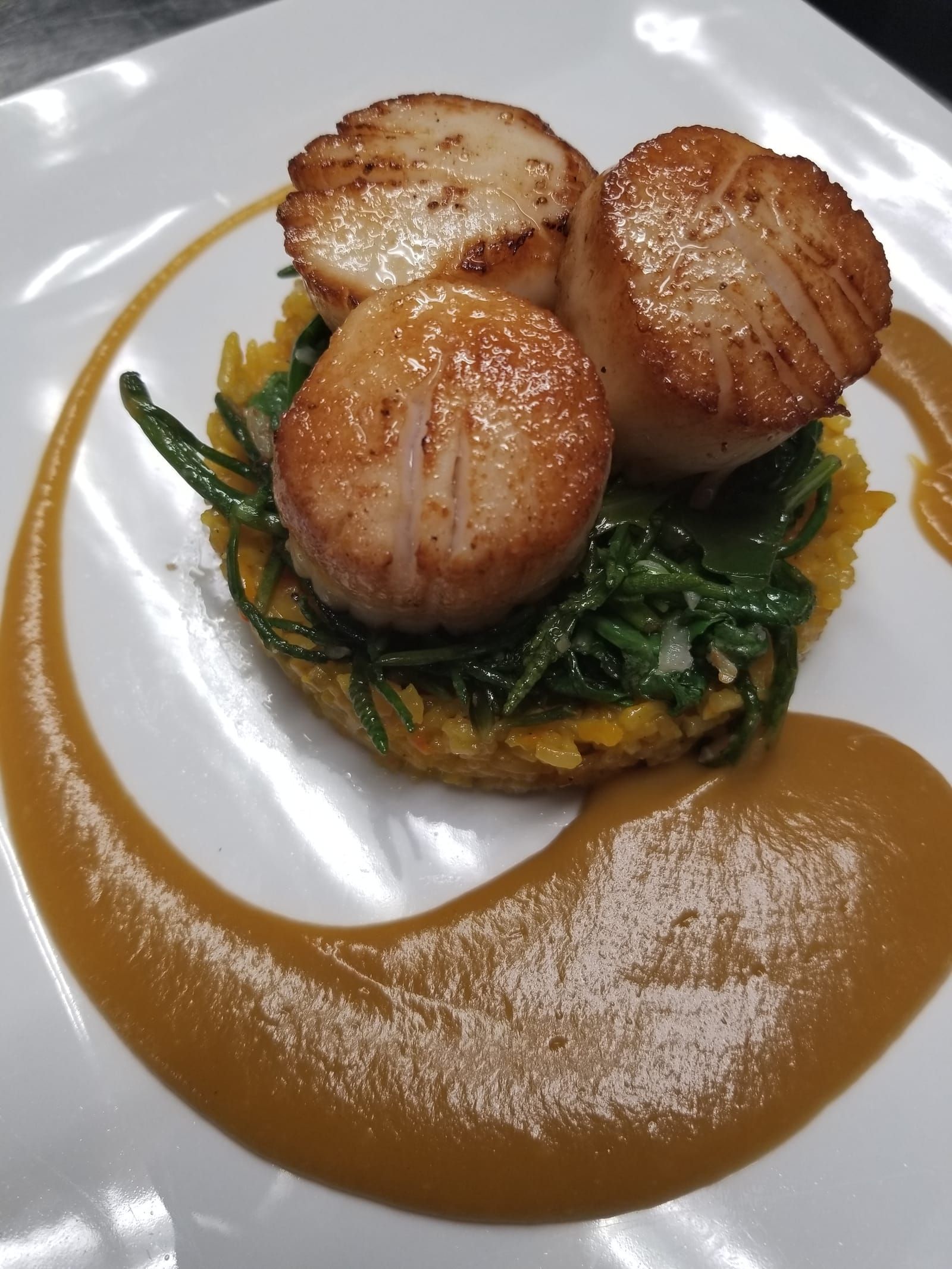 Seared scallops on a bed of saffron rice with greens